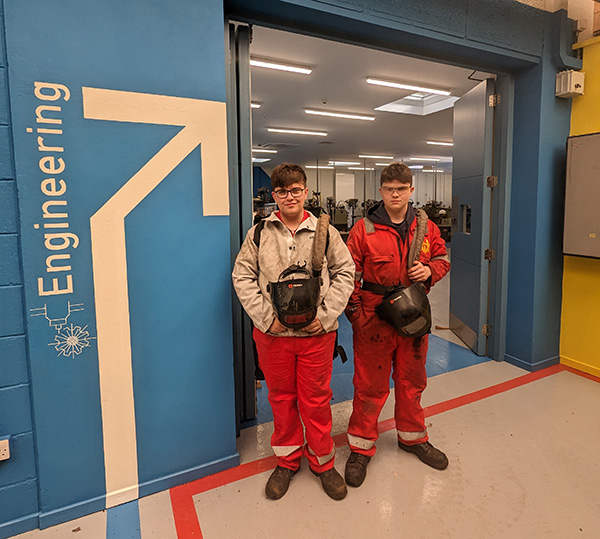 Two students standing with welding helmets